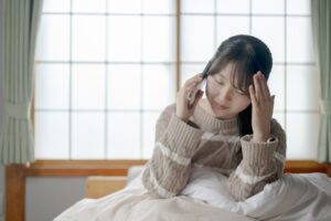 体調不良で頭を押さえキャンセルの電話をしている女性の写真
